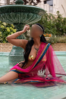 Exotic girl in colourful traditional clothing sitting in a new-classic style fountain